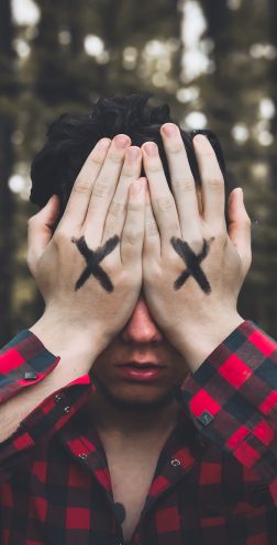 man in red and black plaid dress shirt covering face with hands